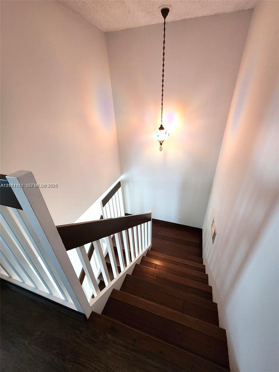 Staircase featuring dark wood-finish treads, a white spindle railing, a dark wood handrail, and a decorative pendant light fixture
