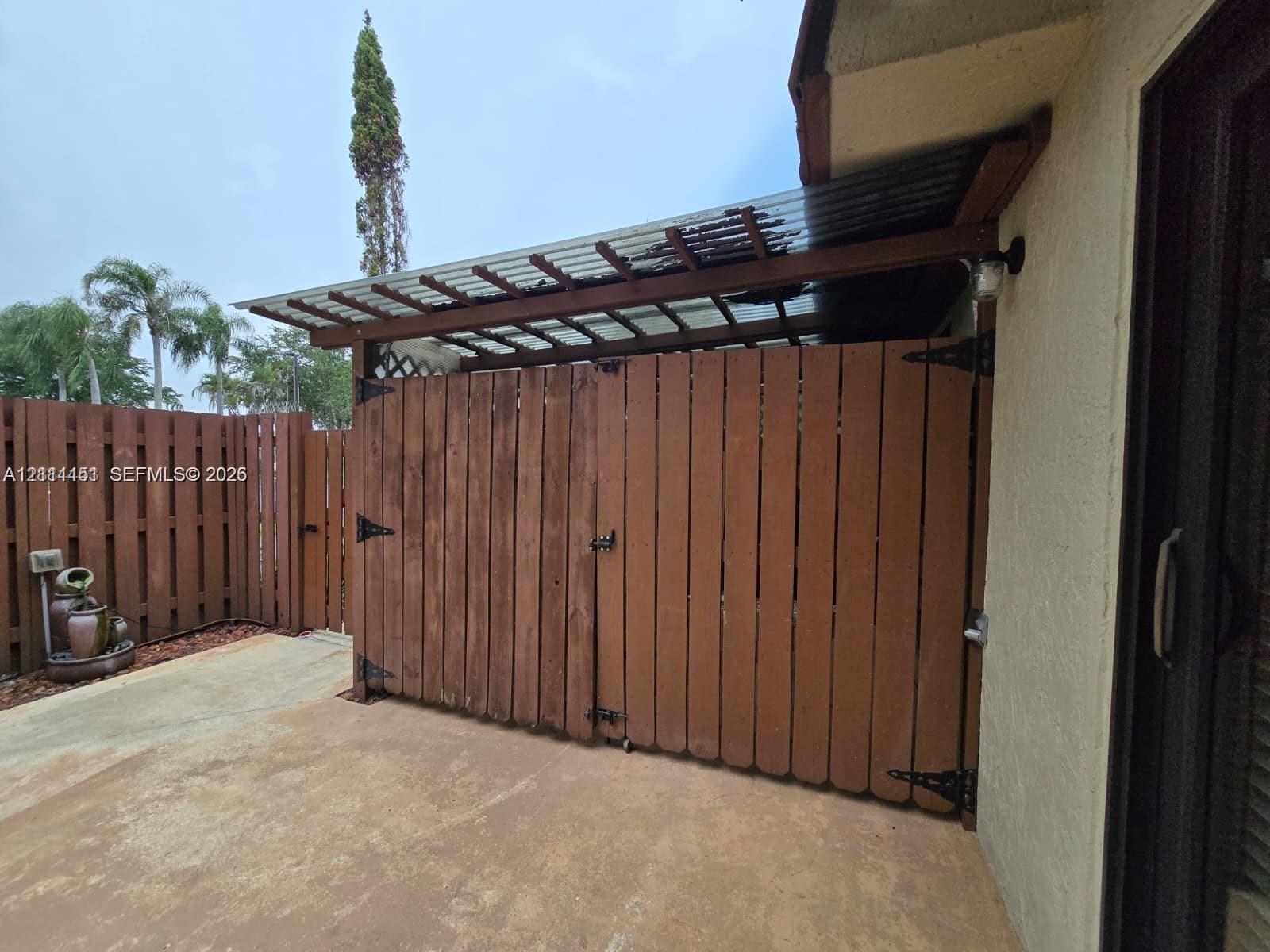 Fenced outdoor storage area featuring vertical wood-plank siding, a corrugated translucent roof covering, and heavy-duty metal hardware Fenced outdoor storage area featuring vertical wood-plank siding, a corrugated translucent roof covering, and heavy-duty metal hardware
