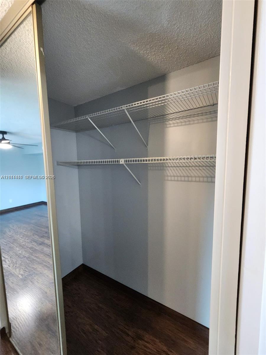 Storage closet featuring floor-to-ceiling mirrored sliding doors, dual-tier wire shelving, and wood-finish flooring