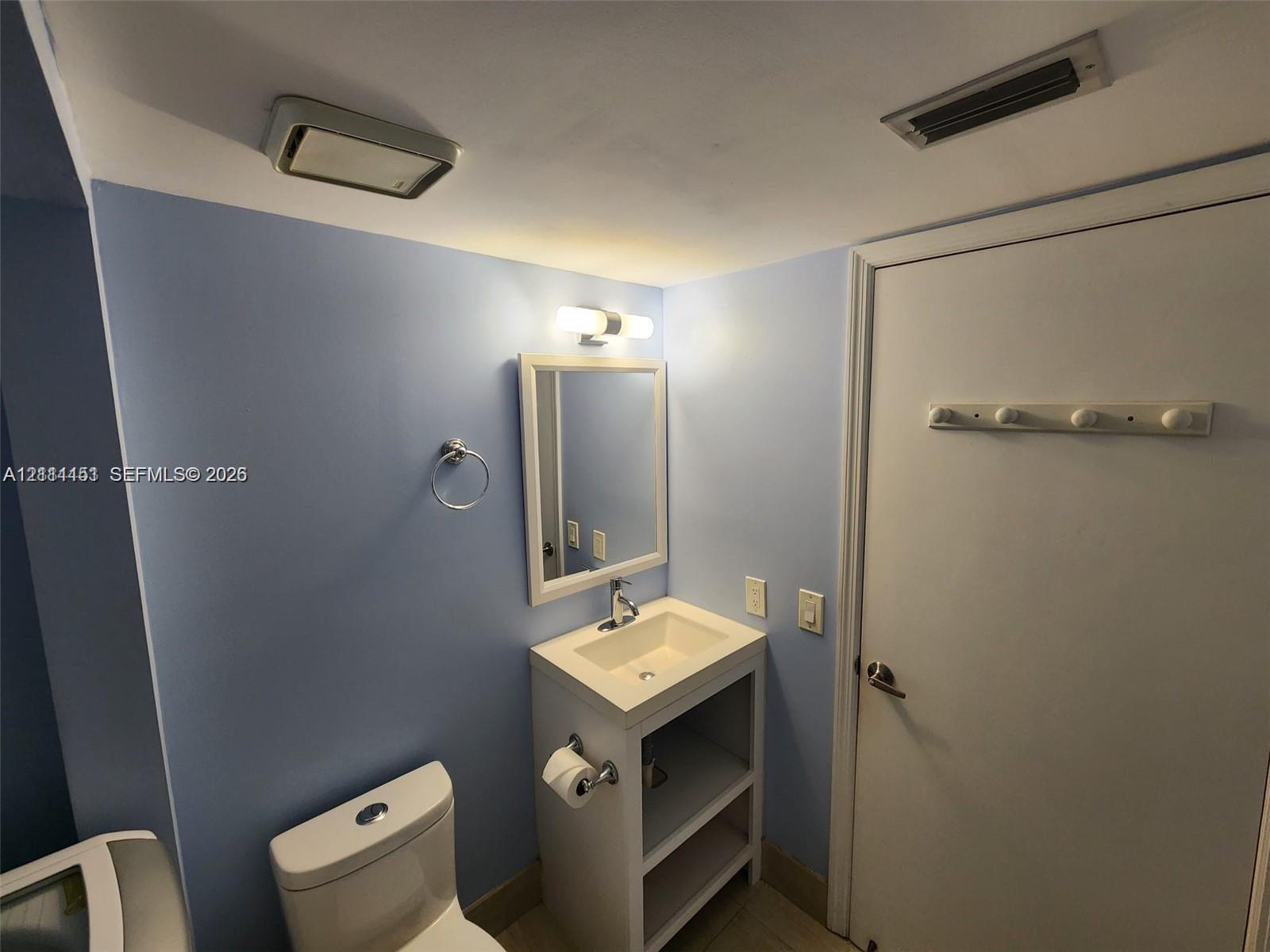 Bathroom featuring a white vanity with an integrated sink, wall-mounted light fixture, rectangular mirror, and dual-flush toilet