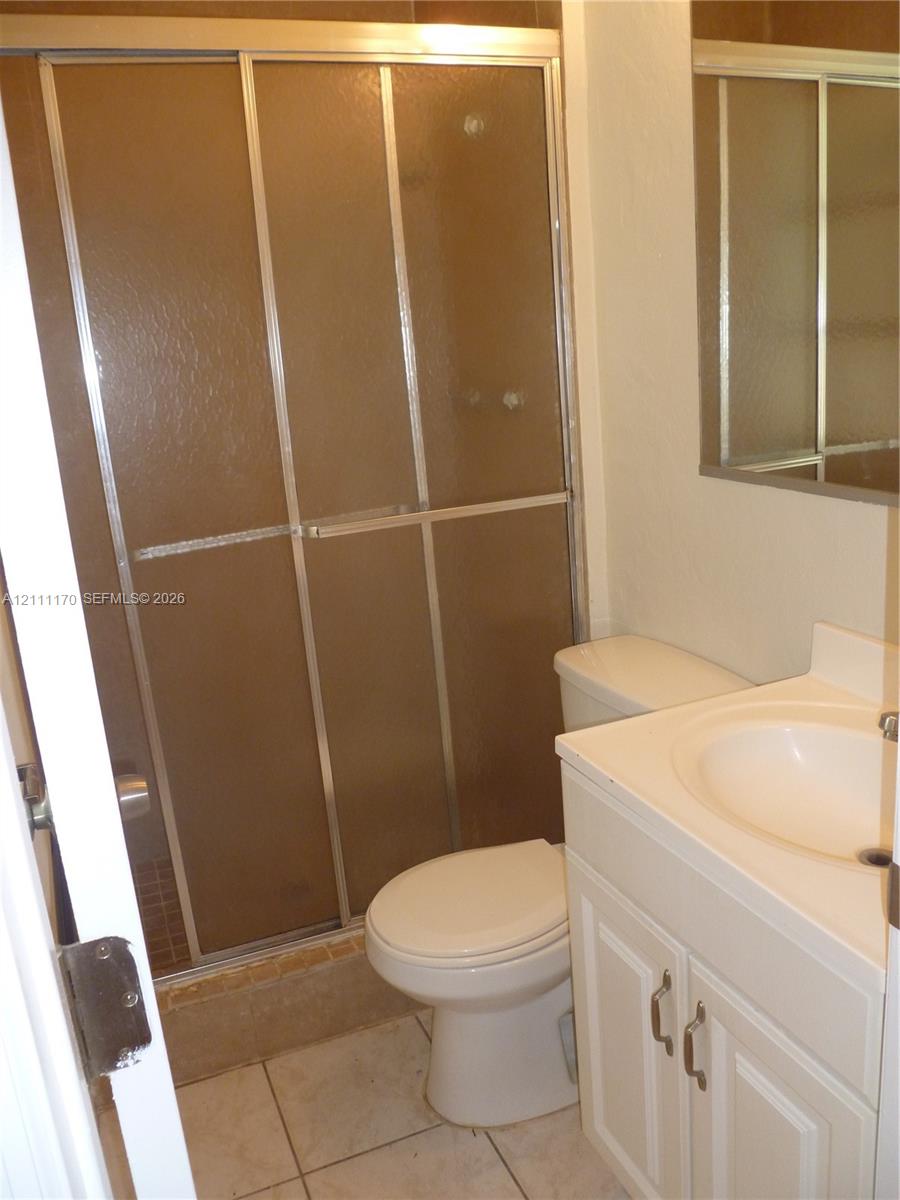 Shower featuring a metal-framed sliding enclosure with textured glass, single-basin vanity with an integrated countertop, wall-mounted mirror, and tile flooring