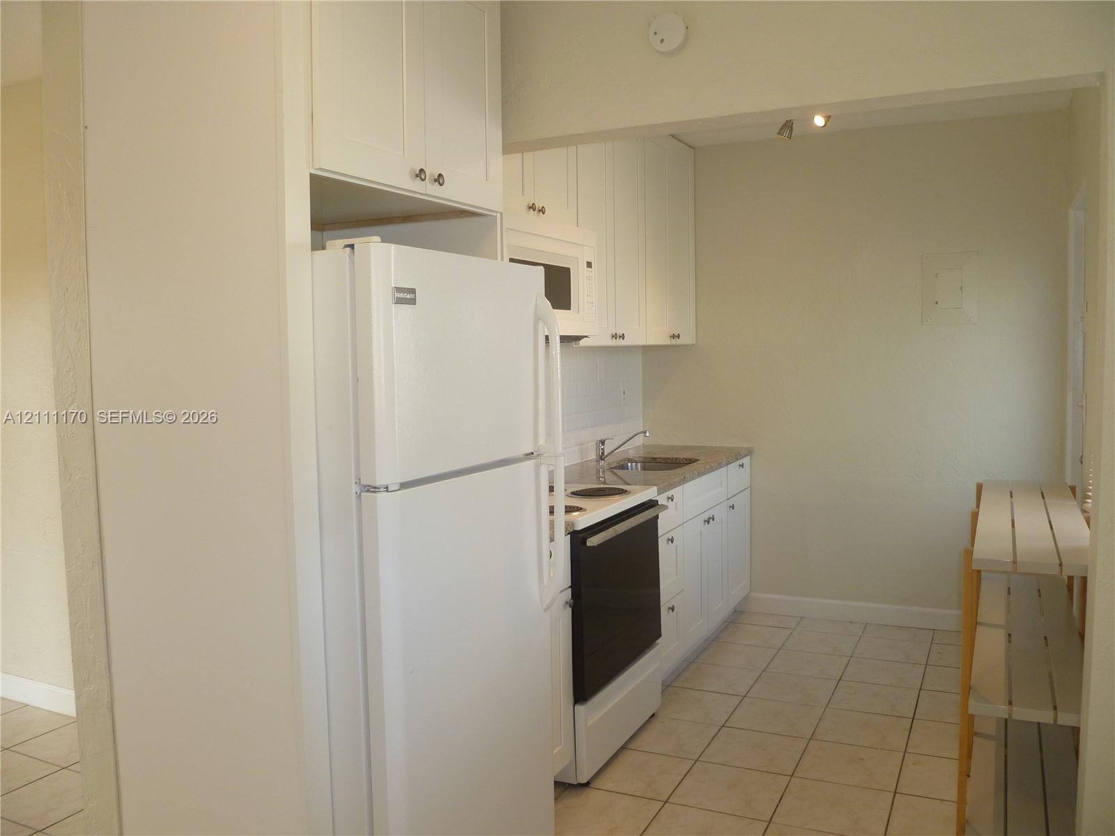 Kitchen featuring white cabinetry, stone-finish countertops, tile flooring, and integrated white appliances