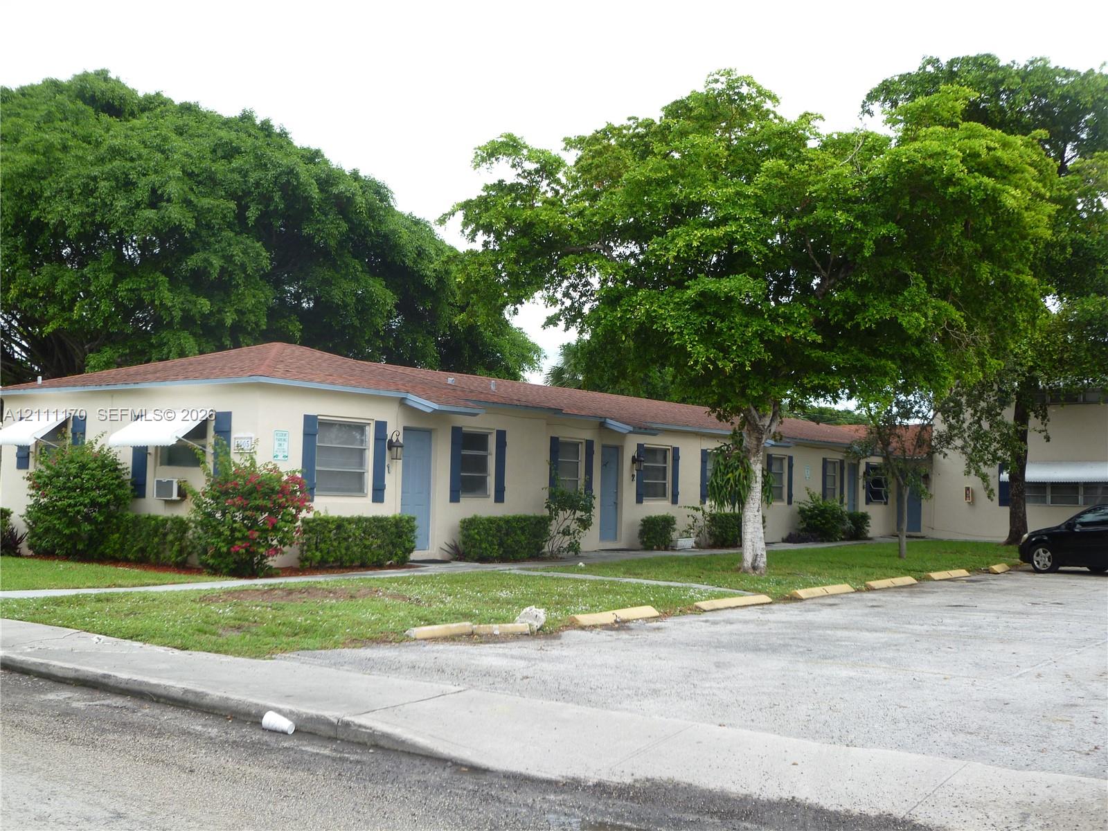 Single-story exterior featuring a hip roof, blue decorative shutters, assigned surface parking, and mature trees Single-story exterior featuring a hip roof, blue decorative shutters, assigned surface parking, and mature trees
