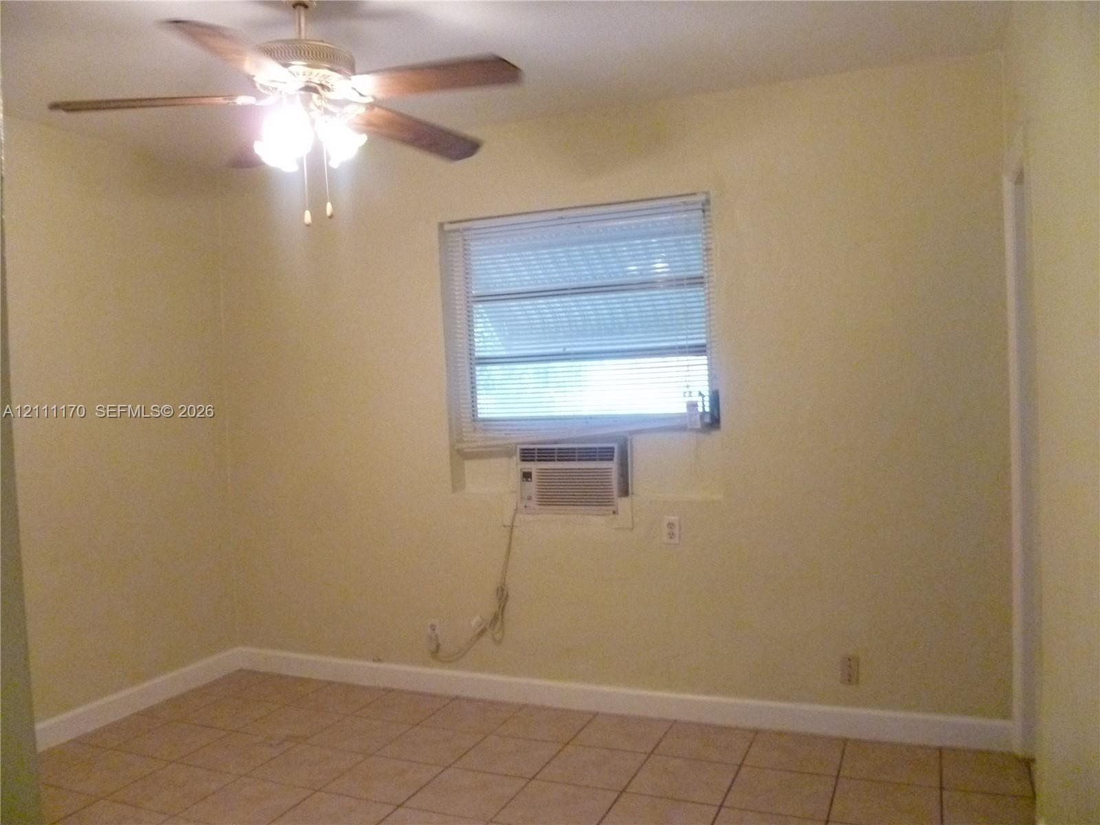Interior space featuring ceramic tile flooring, a multi-blade ceiling fan with integrated lighting, a dual-pane window with horizontal blinds, and a built-in wall air conditioning unit