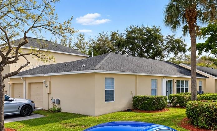Stucco exterior with a multi-hipped asphalt shingle roof, attached two-car garage, and mature landscaping