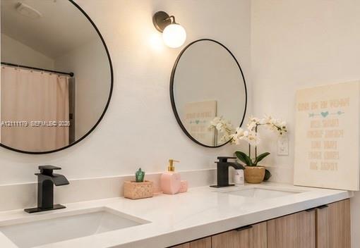Dual-sink vanity featuring a white solid-surface countertop, wood-finish cabinetry, matte black hardware, and two circular wall-mounted mirrors