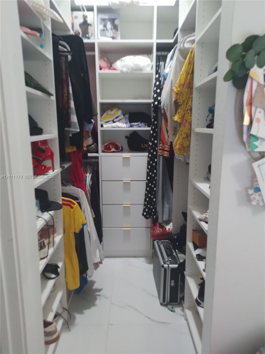 Walk-in closet featuring white custom built-in shelving, four integrated storage drawers, and white tile flooring