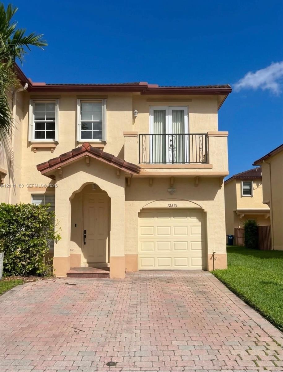 Stucco exterior with an arched entryway, paver driveway, single-car garage, and second-story balcony with metal railing