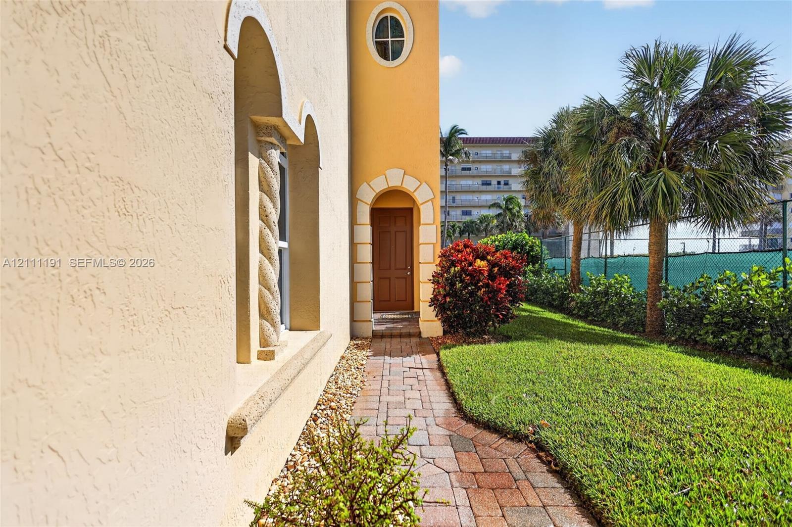 Stucco exterior featuring an arched entrance with decorative masonry surrounds, a spiral column detail, an oval window, and a paver walkway
