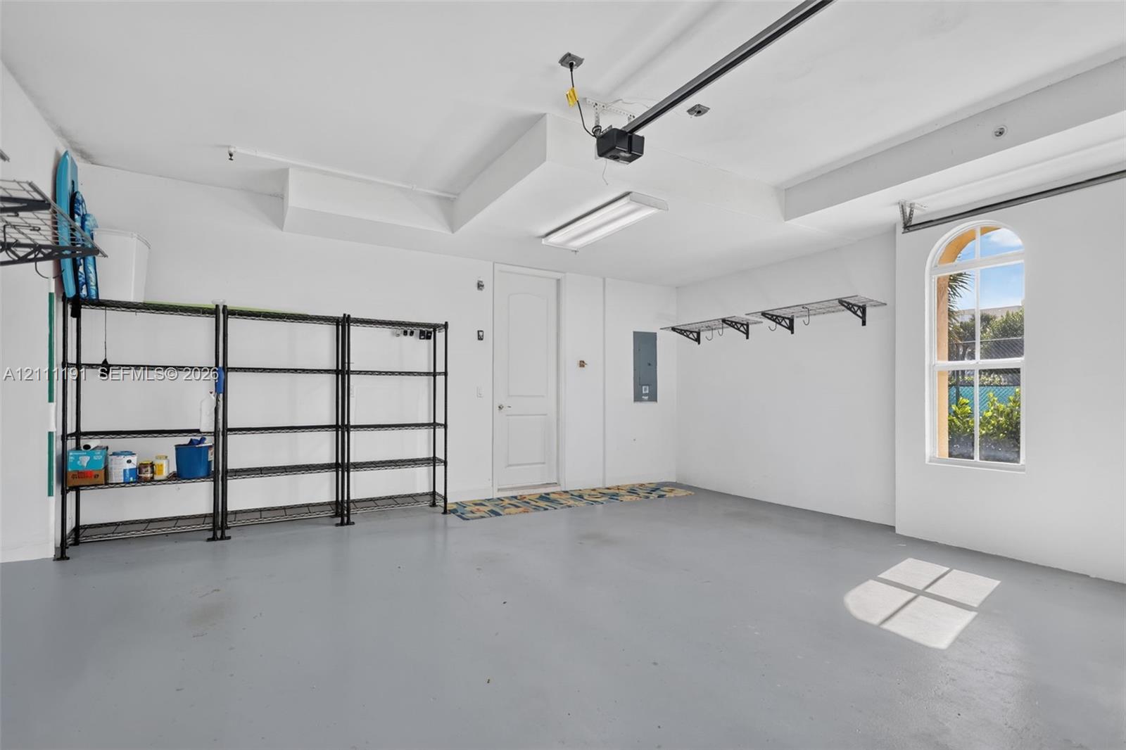 2 car Garage featuring a painted concrete floor, arched window, and overhead fluorescent lighting