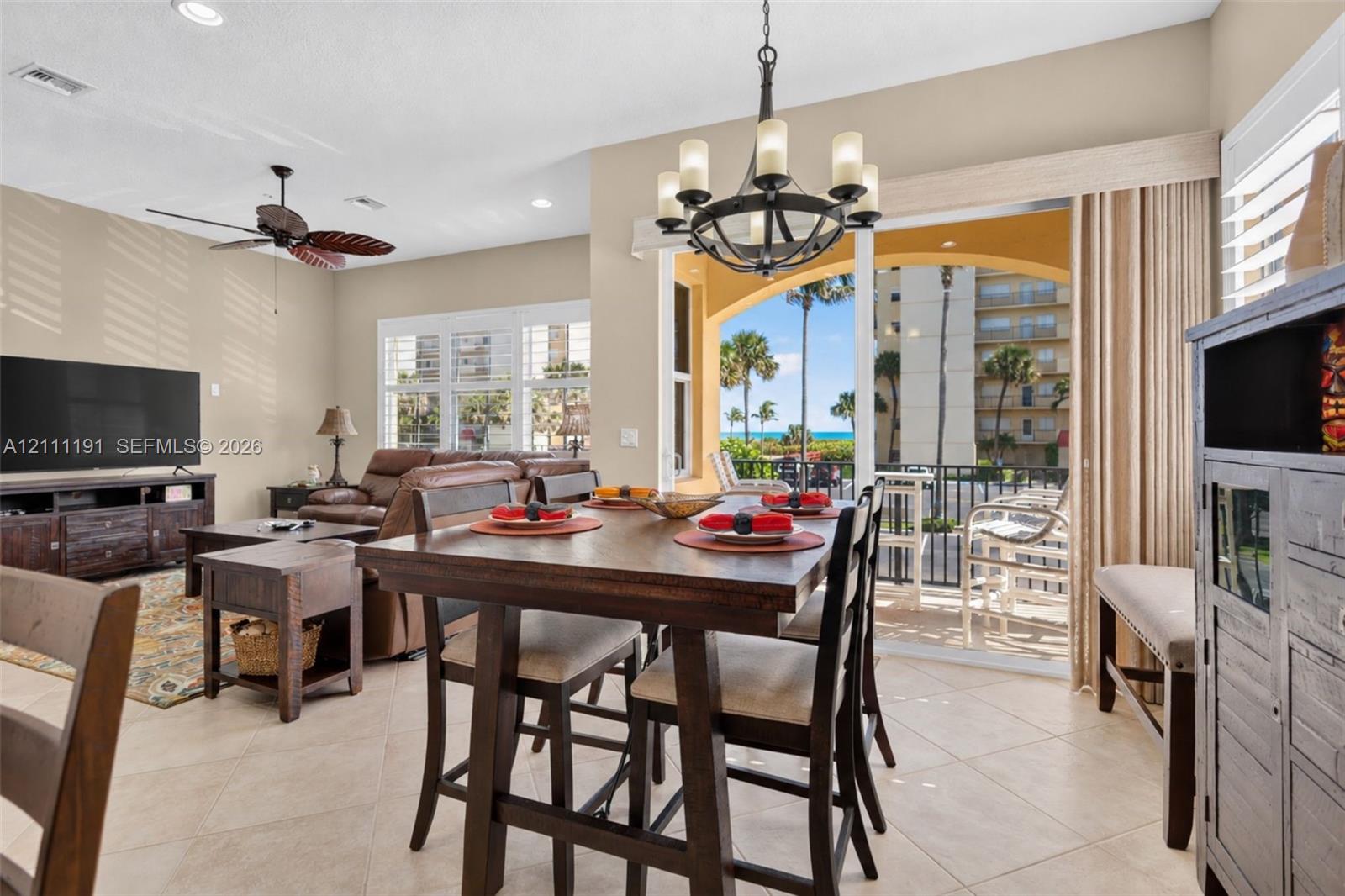 Open-concept living space featuring neutral tile flooring, recessed lighting, a ceiling fan, a multi-arm chandelier, and sliding glass doors opening to a covered balcony