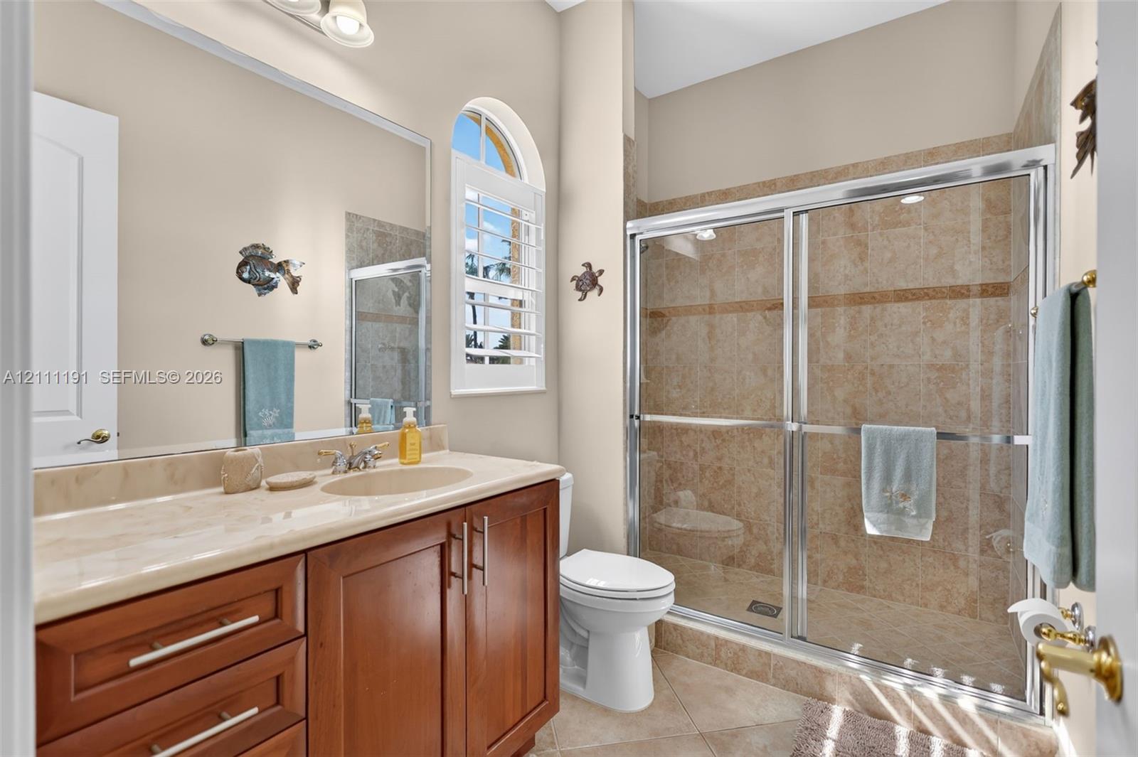 2nd floor Bathroom featuring wood-finish cabinetry, stone countertop, arched window with plantation shutters, and a walk-in shower with stone tile surround and sliding glass doors