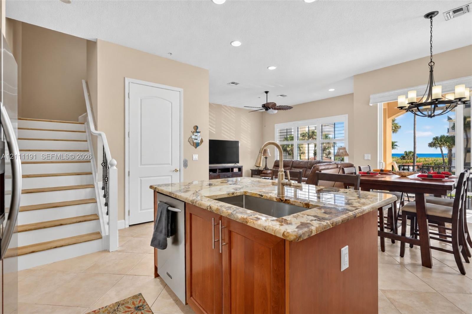 Kitchen island featuring a stone countertop, under-mount stainless steel sink, and wood cabinetry, complemented by tile flooring and an open-concept layout