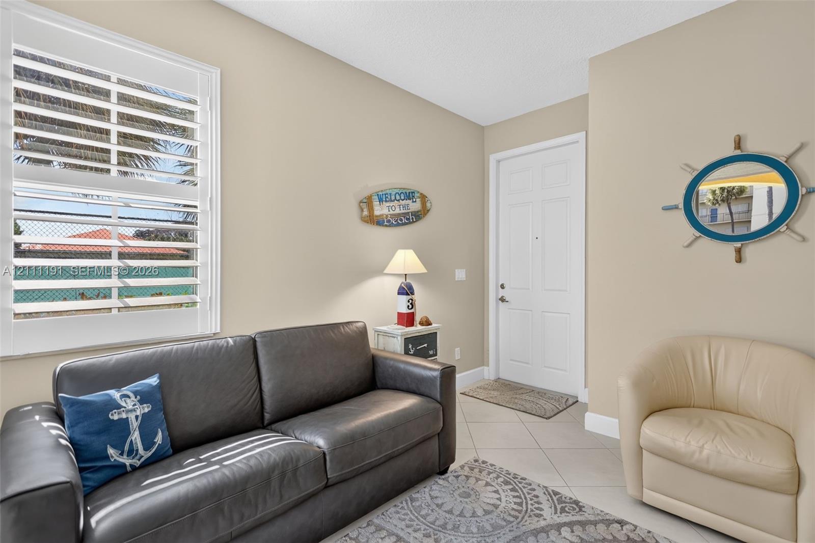 Extra sitting area/foyer on the first floor upon entering the front door. Neutral-toned interior featuring large-format ceramic tile flooring, adjustable white plantation shutters, and a six-panel door with brushed nickel hardware