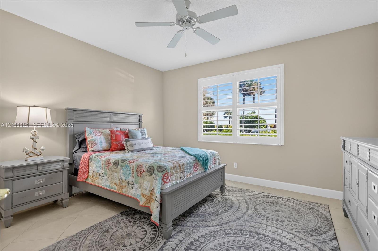 3rd Bedroom on 1st floor. Neutral-toned room featuring a central ceiling fan with light fixture, large plantation shutters, and light-colored tile flooring