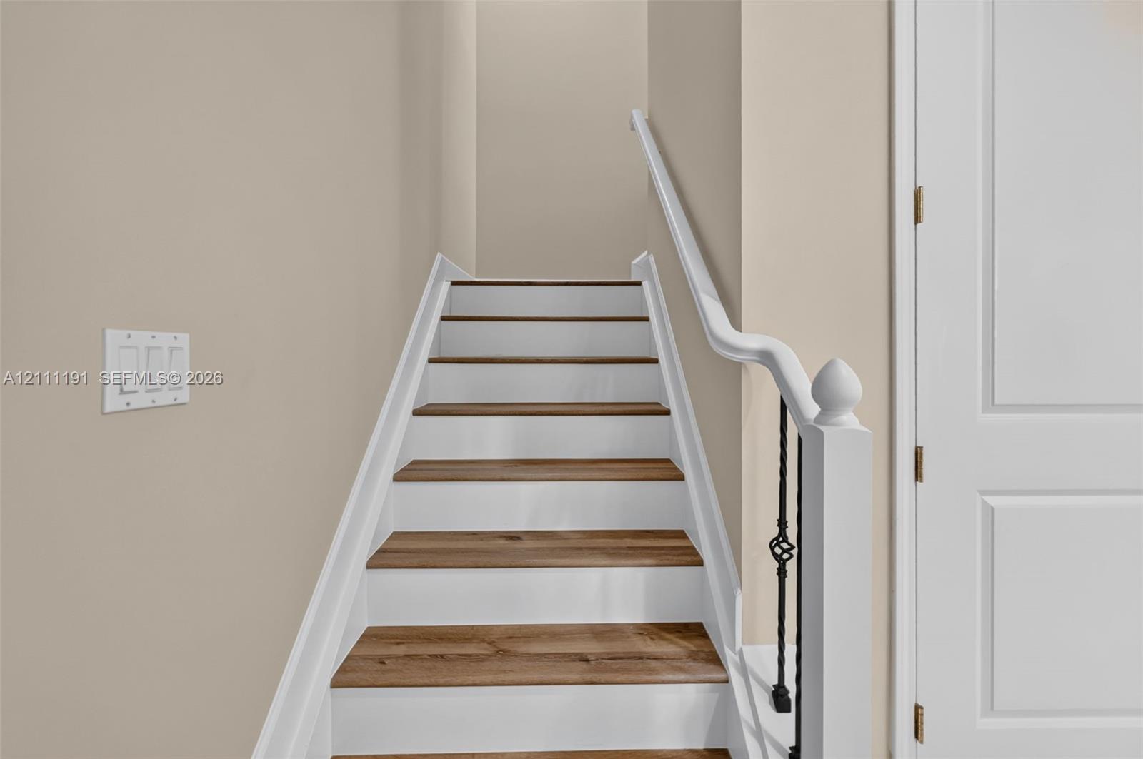 Staircase to the living area featuring wood-finish treads, white painted risers, ornate metal balusters, and a white handrail