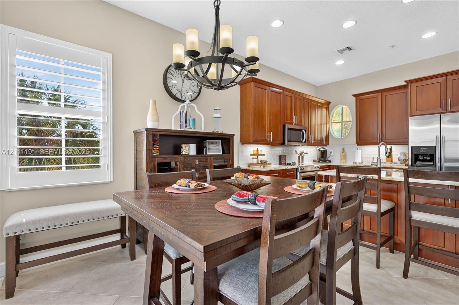 Kitchen featuring wood cabinetry, stainless steel appliances, recessed ceiling lighting, a decorative chandelier, and tile flooring
