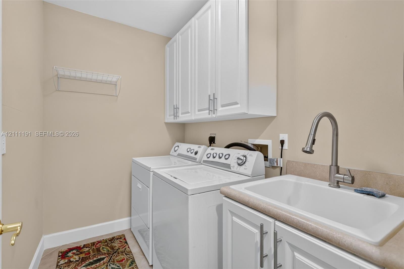Laundry room featuring white Shaker-style upper cabinetry, a utility sink with a high-arch pull-down faucet, solid surface countertop, and wall-mounted wire shelving