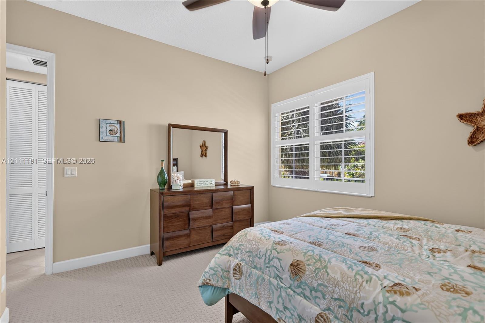 Neutral-toned walls featuring a ceiling fan with integrated lighting, white louvered plantation shutters, and a closet with bifold louvered doors