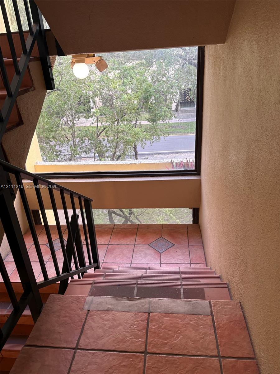 Staircase featuring textured terracotta-toned tile flooring, diamond-patterned tile accents, and black metal railings