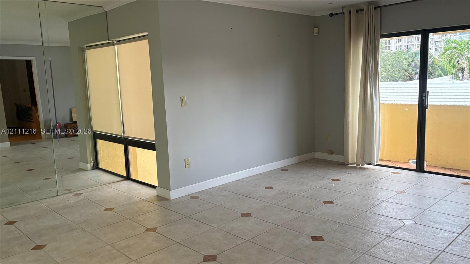 Living area featuring large-format tile flooring with decorative inlay accents, expansive wall-to-wall mirror paneling, fixed window panes with integrated blinds, and a sliding glass door providing external access
