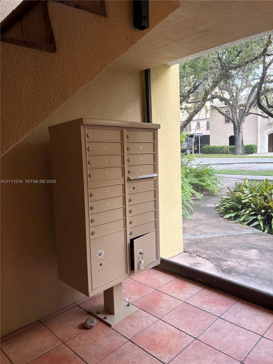 Covered mail station featuring a tan metal multi-unit mailbox console situated on terracotta-style tile flooring