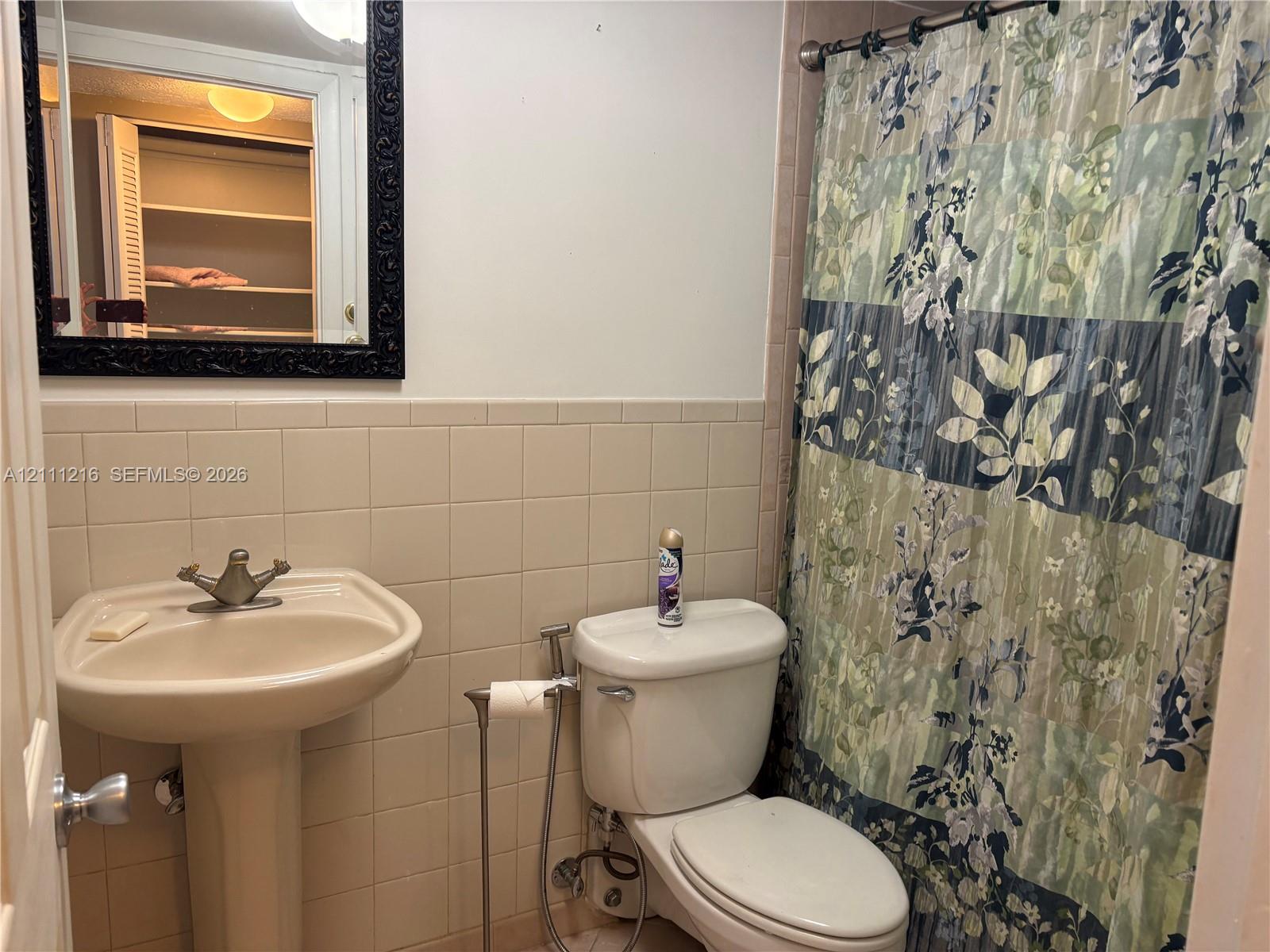 Bathroom featuring a pedestal sink with a metallic faucet, ceramic tile backsplash, and a wall-mounted mirror