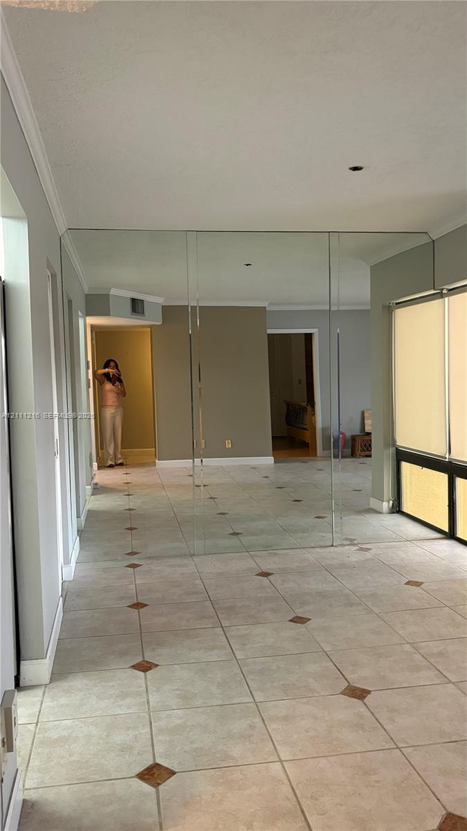 Tile flooring with decorative inset accents, wall-to-wall mirrored paneling, and large windows with horizontal blinds
