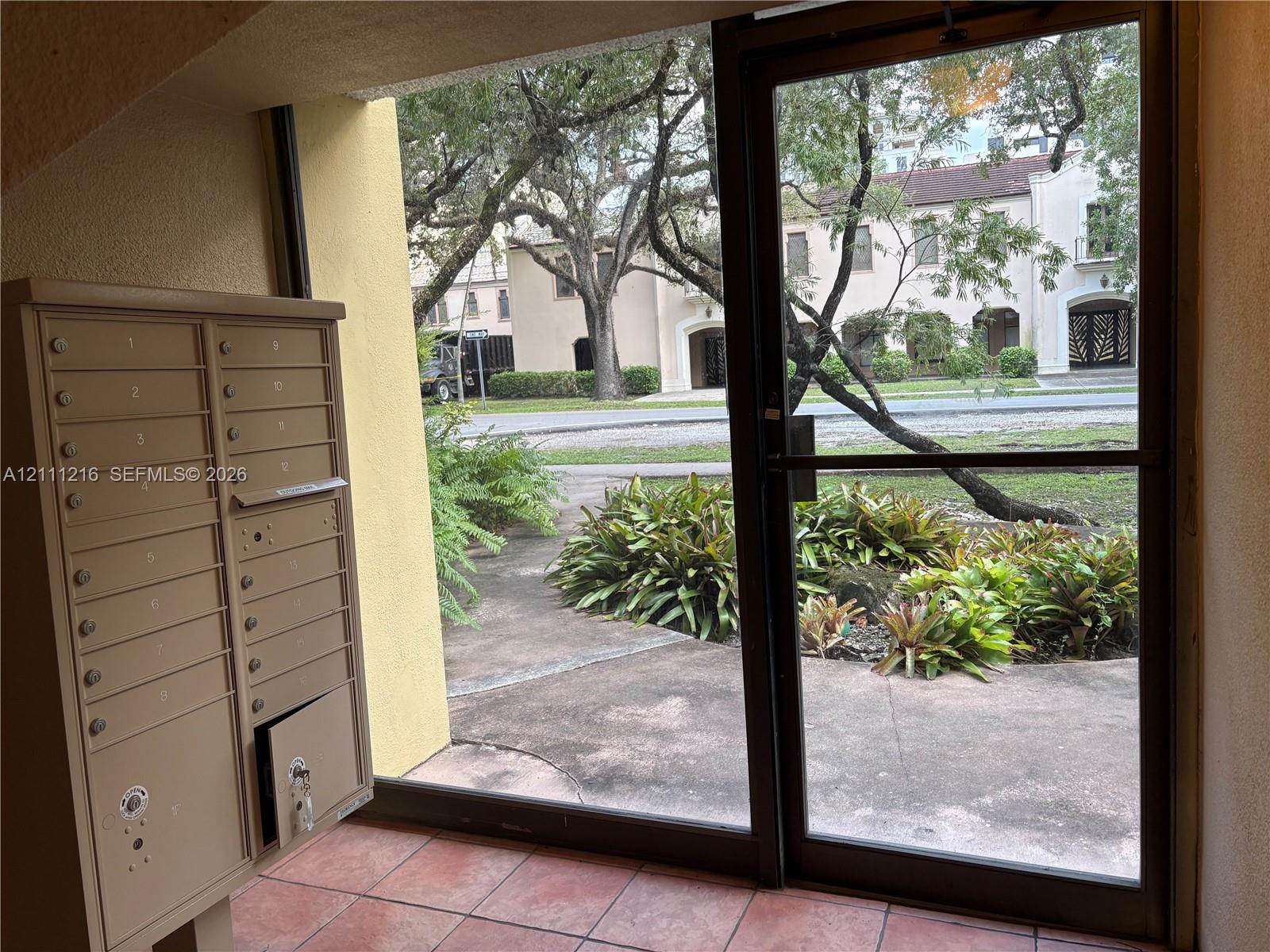 Covered entryway featuring tile flooring, metal mail collection station, and a full-light glass door