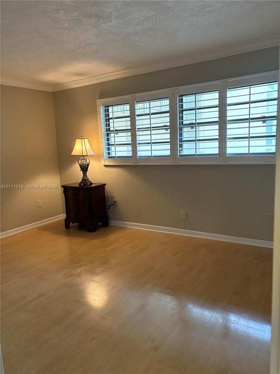 Interior space featuring wood-finish flooring, multi-pane windows with integrated white plantation shutters, and crown molding
