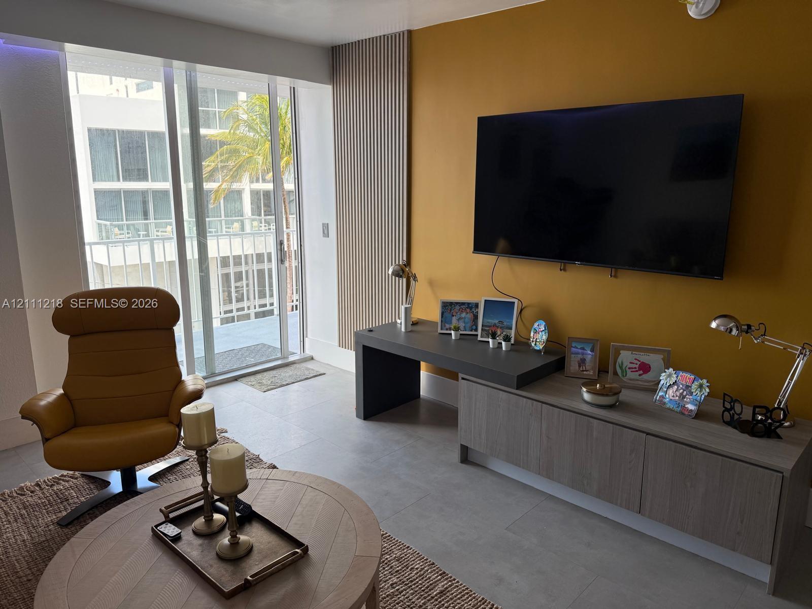 Living area featuring floor-to-ceiling glass sliding doors, accent wall with vertical slat paneling, and large-format tile flooring Living area featuring floor-to-ceiling glass sliding doors, accent wall with vertical slat paneling, and large-format tile flooring