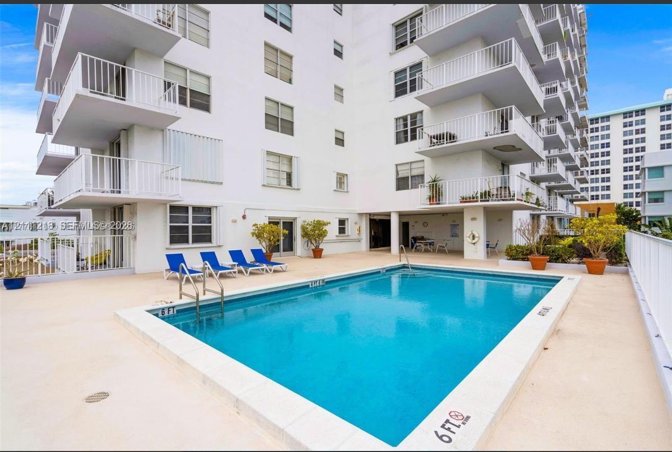 In-ground swimming pool featuring a concrete deck, metal ladder access, and multi-story building exterior with private balcony access