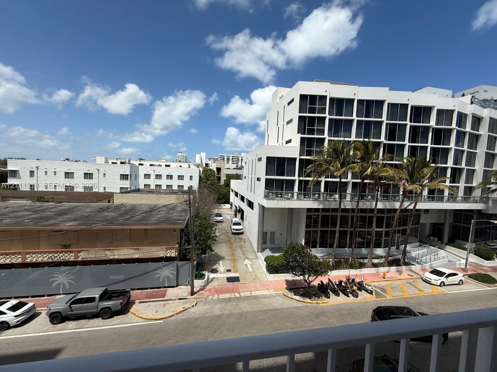 Elevated balcony featuring a white railing, overlooking an urban streetscape with multi-story buildings, palm trees, and clear sky Elevated balcony featuring a white railing, overlooking an urban streetscape with multi-story buildings, palm trees, and clear sky