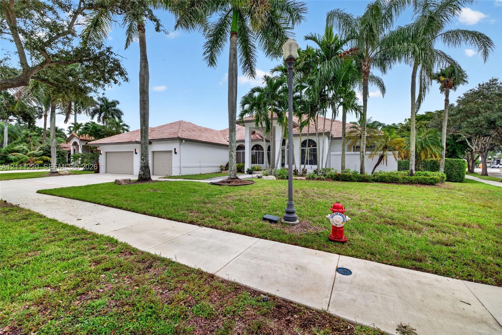 Single-story residence featuring a tile roof, light-toned exterior finish, attached two-car garage, concrete driveway, and mature palm landscaping