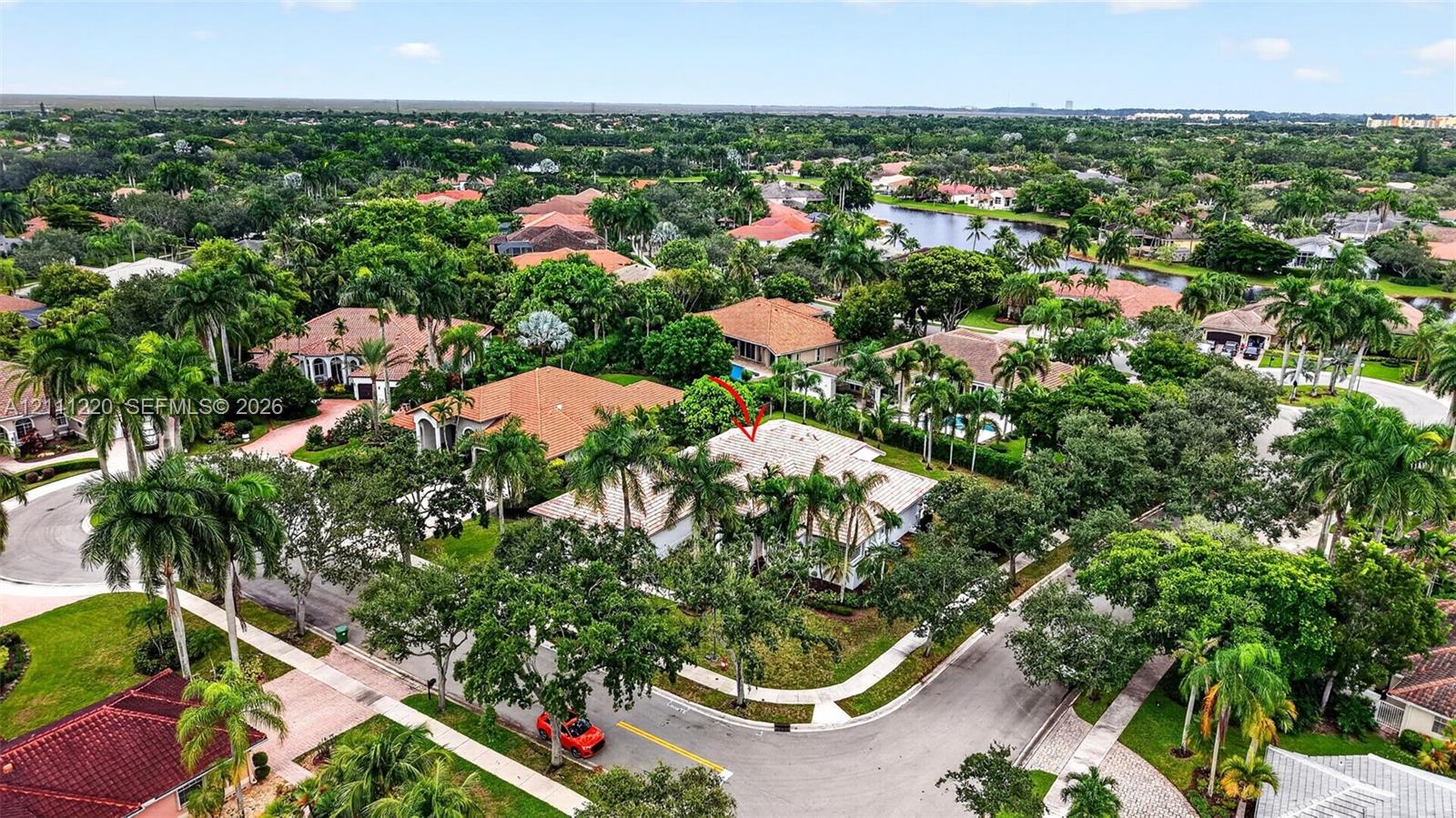 Aerial perspective of a corner lot residence featuring a tile roof, paved driveway, established perimeter landscaping, and mature palm trees