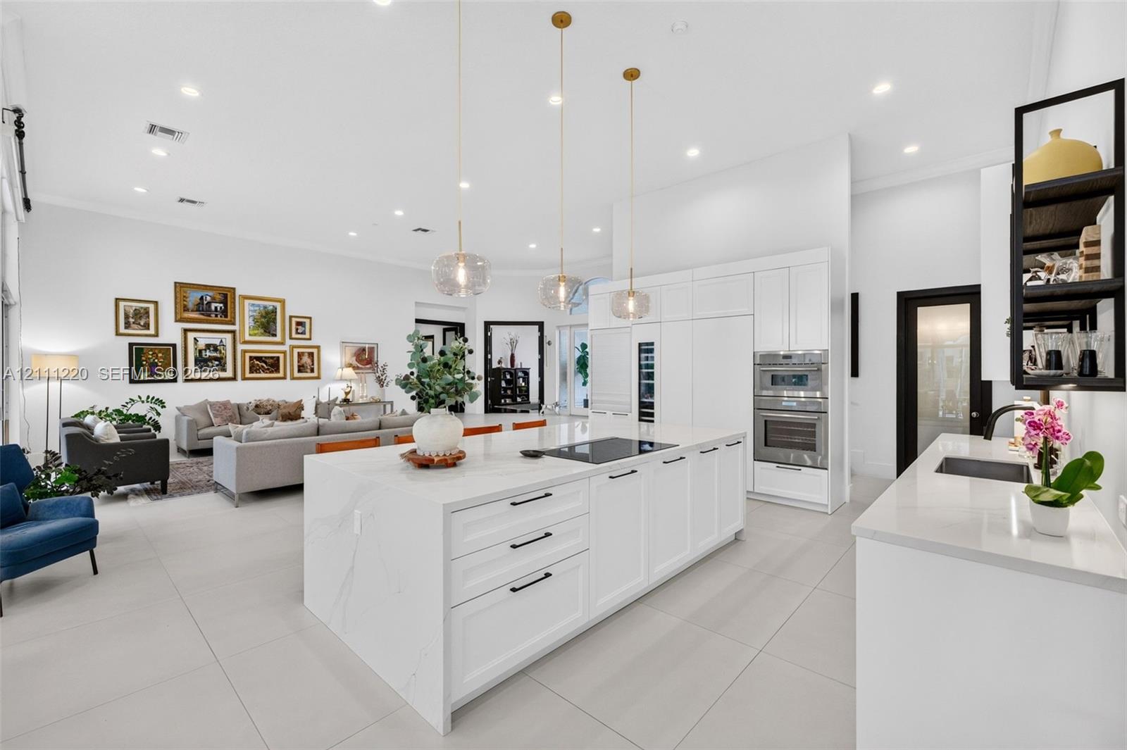 Kitchen featuring a large central island with quartz surfacing, white shaker-style cabinetry, stainless steel double wall ovens, three glass pendant light fixtures, and neutral oversized tile flooring