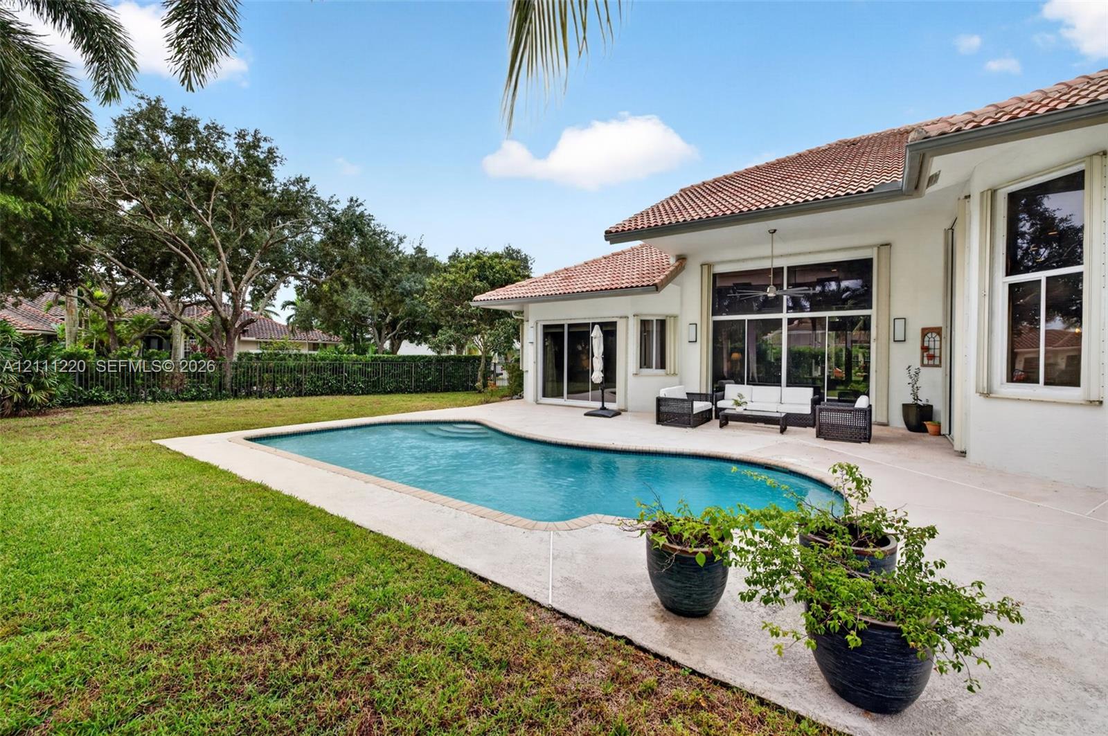 Rear exterior featuring a swimming pool, expansive concrete patio, manicured lawn, tile roof, and floor-to-ceiling glass doors