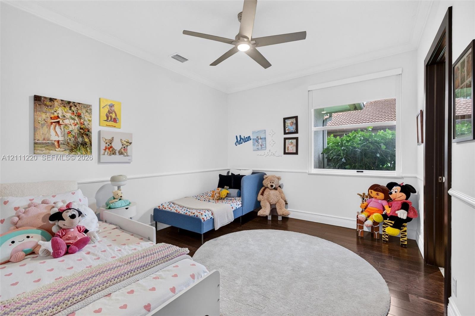 Bedroom interior featuring dark wood-finish flooring, crown molding, chair rail trim, a multi-blade ceiling fan with integrated lighting, and a single-pane window