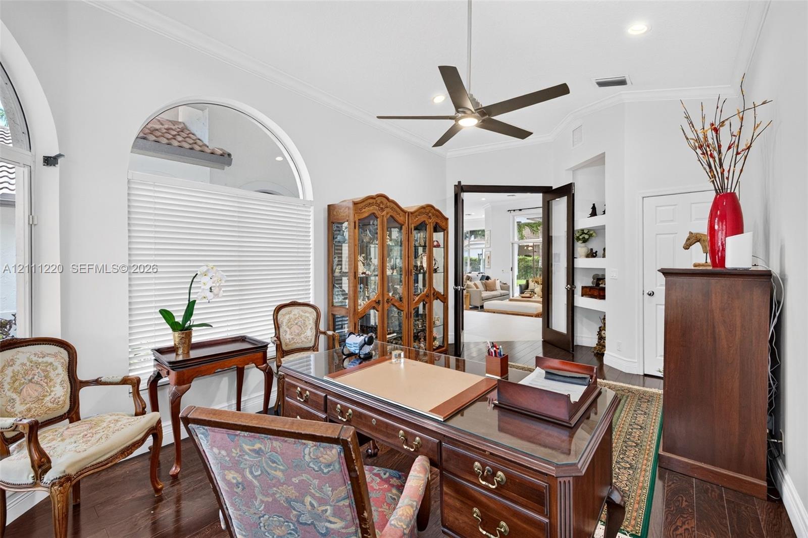 Room featuring arched windows, dark wood-finish flooring, built-in recessed shelving, and a ceiling fan