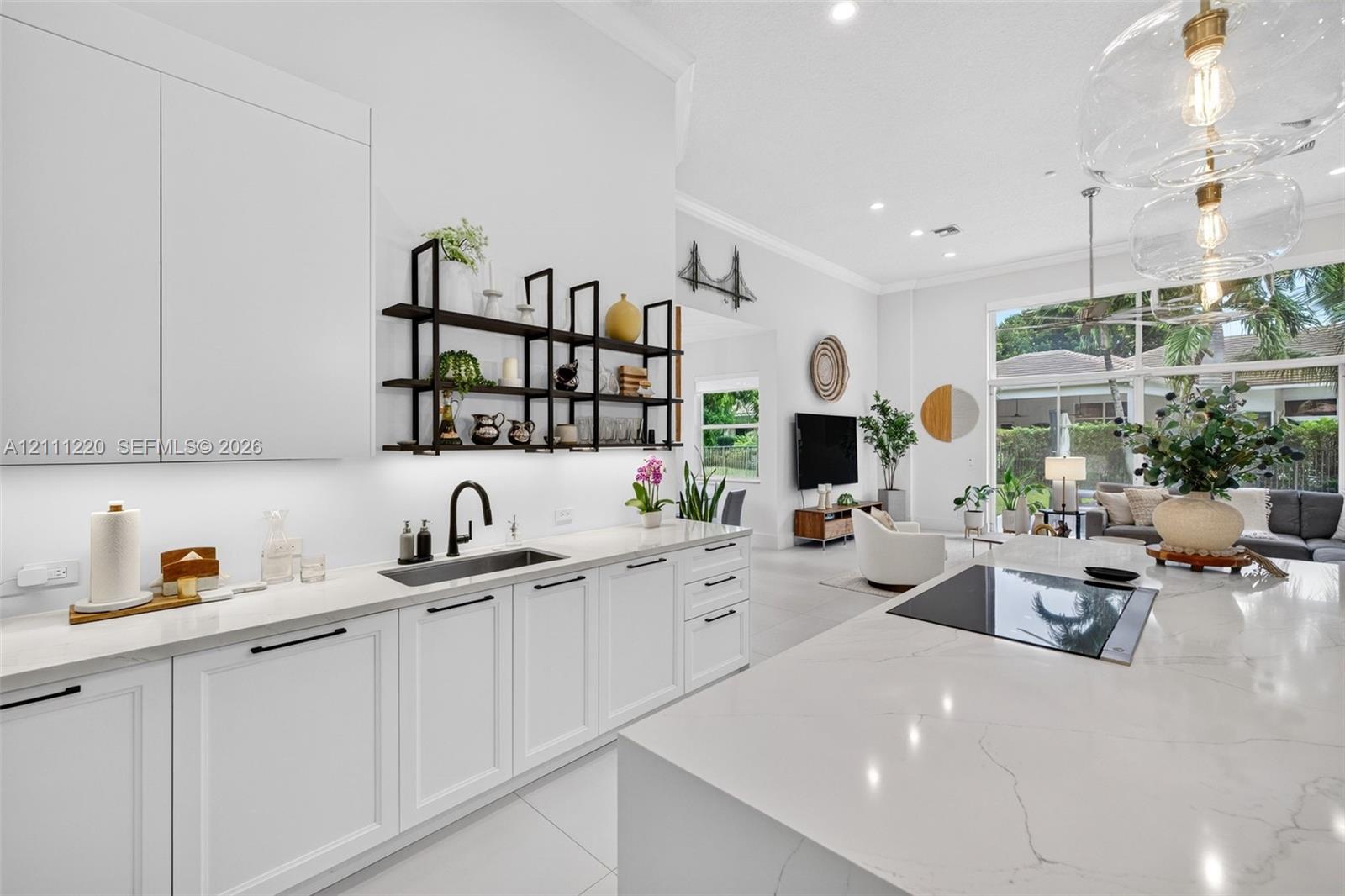 Kitchen featuring white shaker-style cabinetry, a large central island with a solid surface countertop, matte black hardware, under-cabinet lighting, and built-in glass pendant illumination