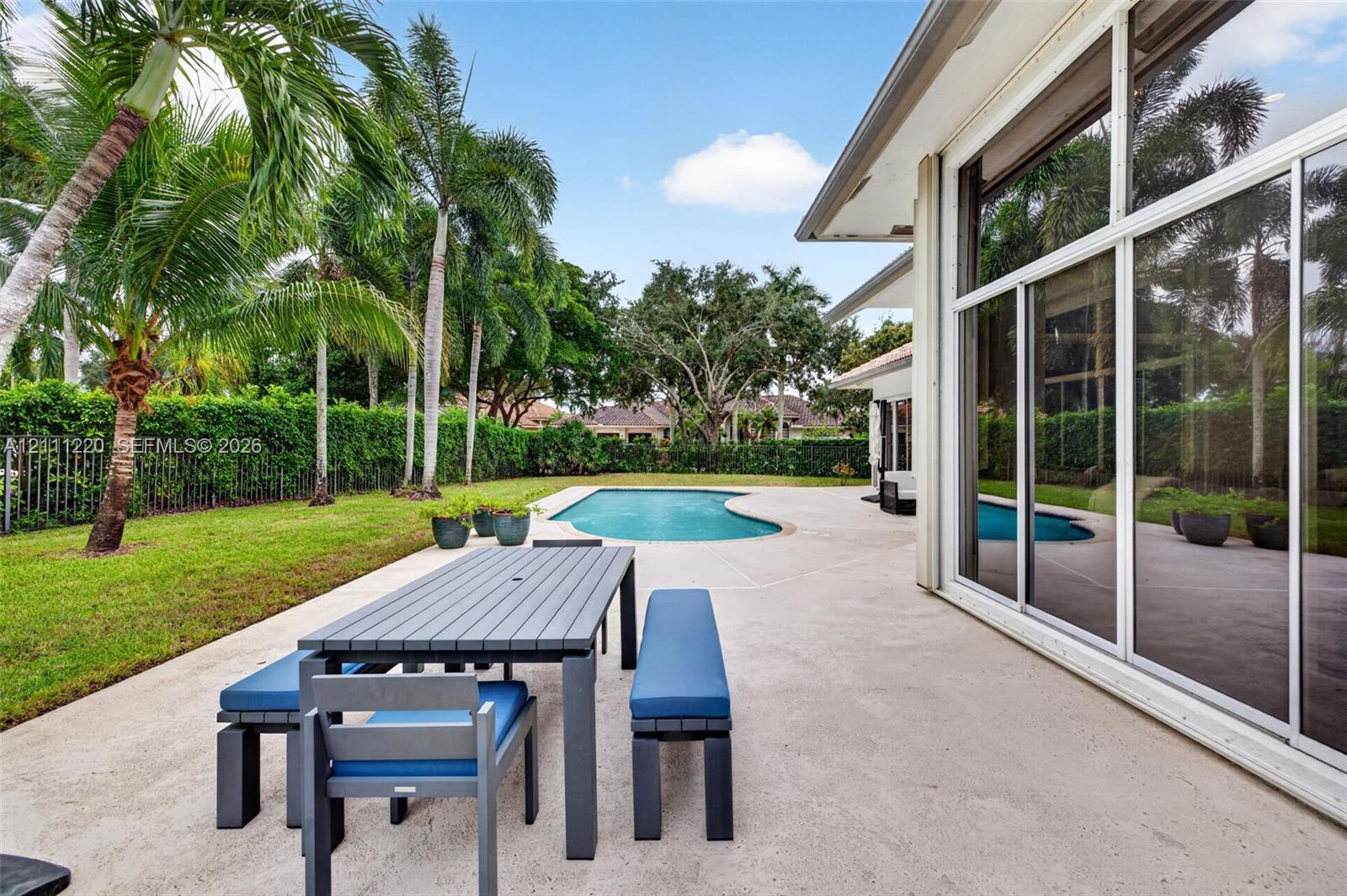 Rear patio featuring expansive concrete decking, in-ground swimming pool, palm trees, and full-height sliding glass doors