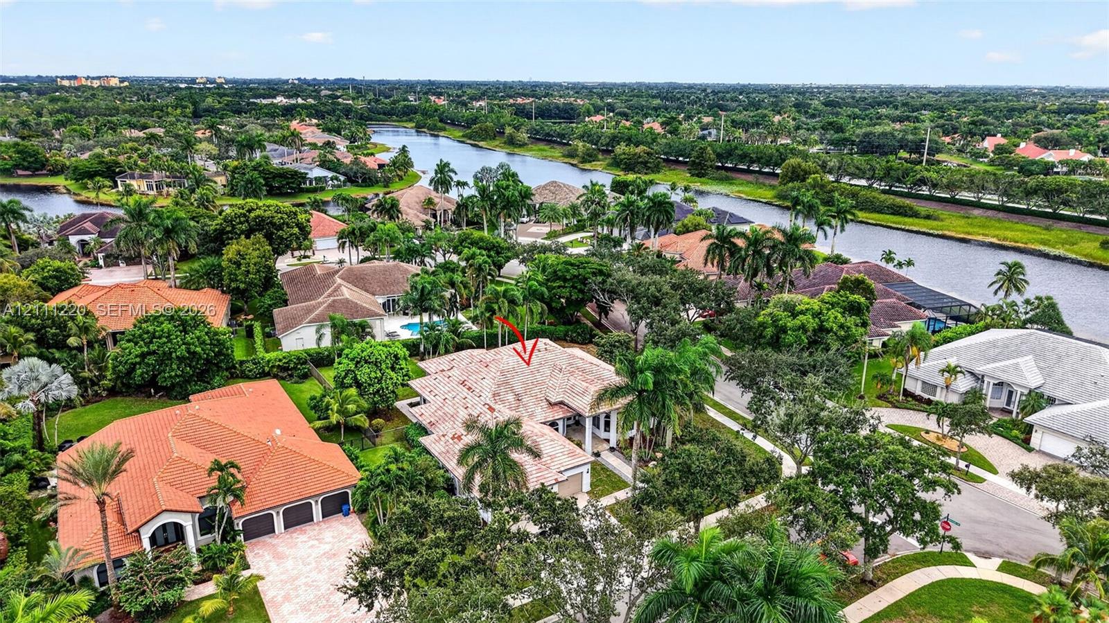 Aerial perspective of a multi-hip tile roof residence featuring a paved driveway, multi-car garage, covered entryway, and mature palm landscaping
