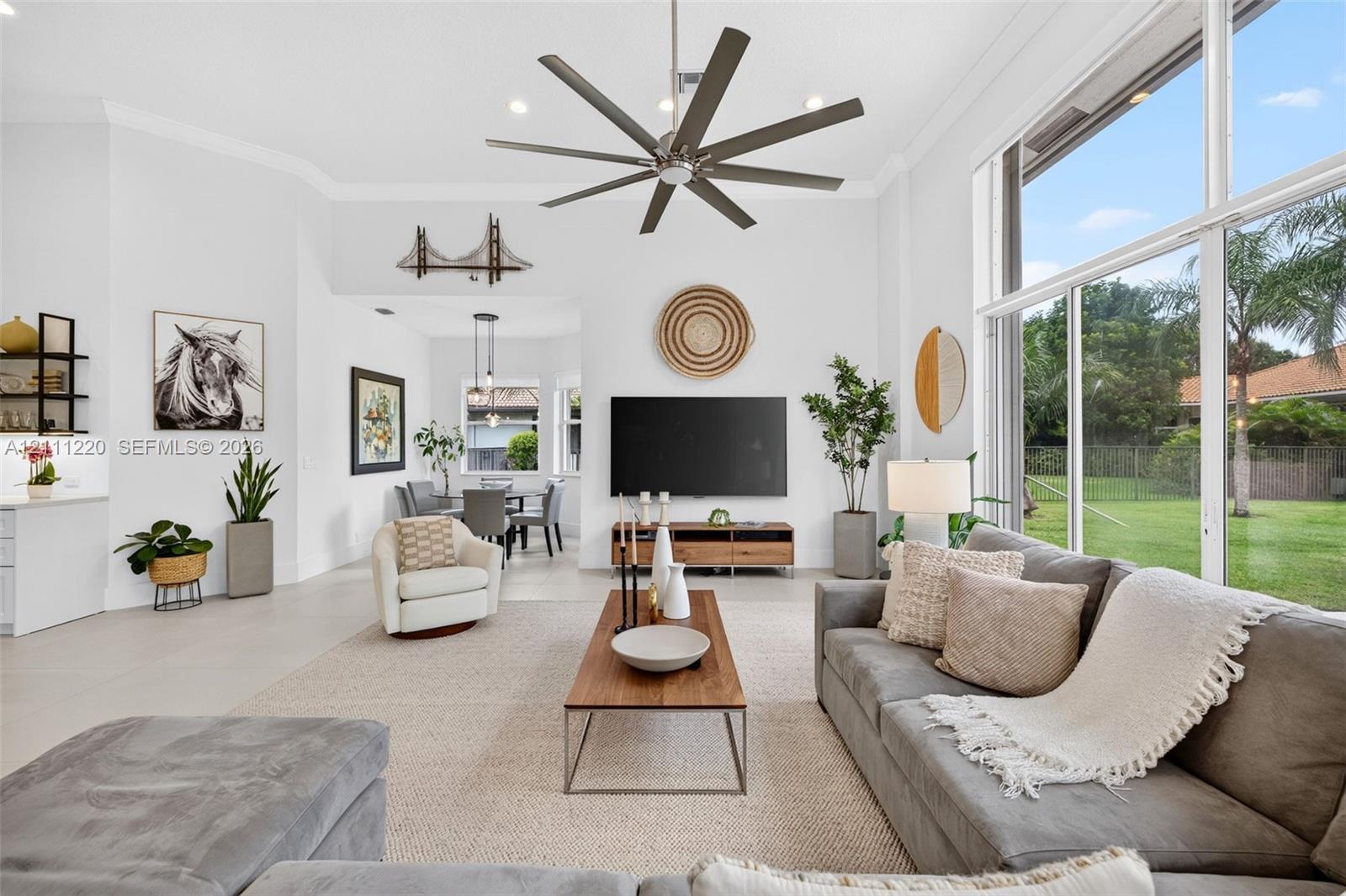 High ceilings featuring a large multi-blade ceiling fan, expansive floor-to-ceiling windows, and neutral oversized floor tiling