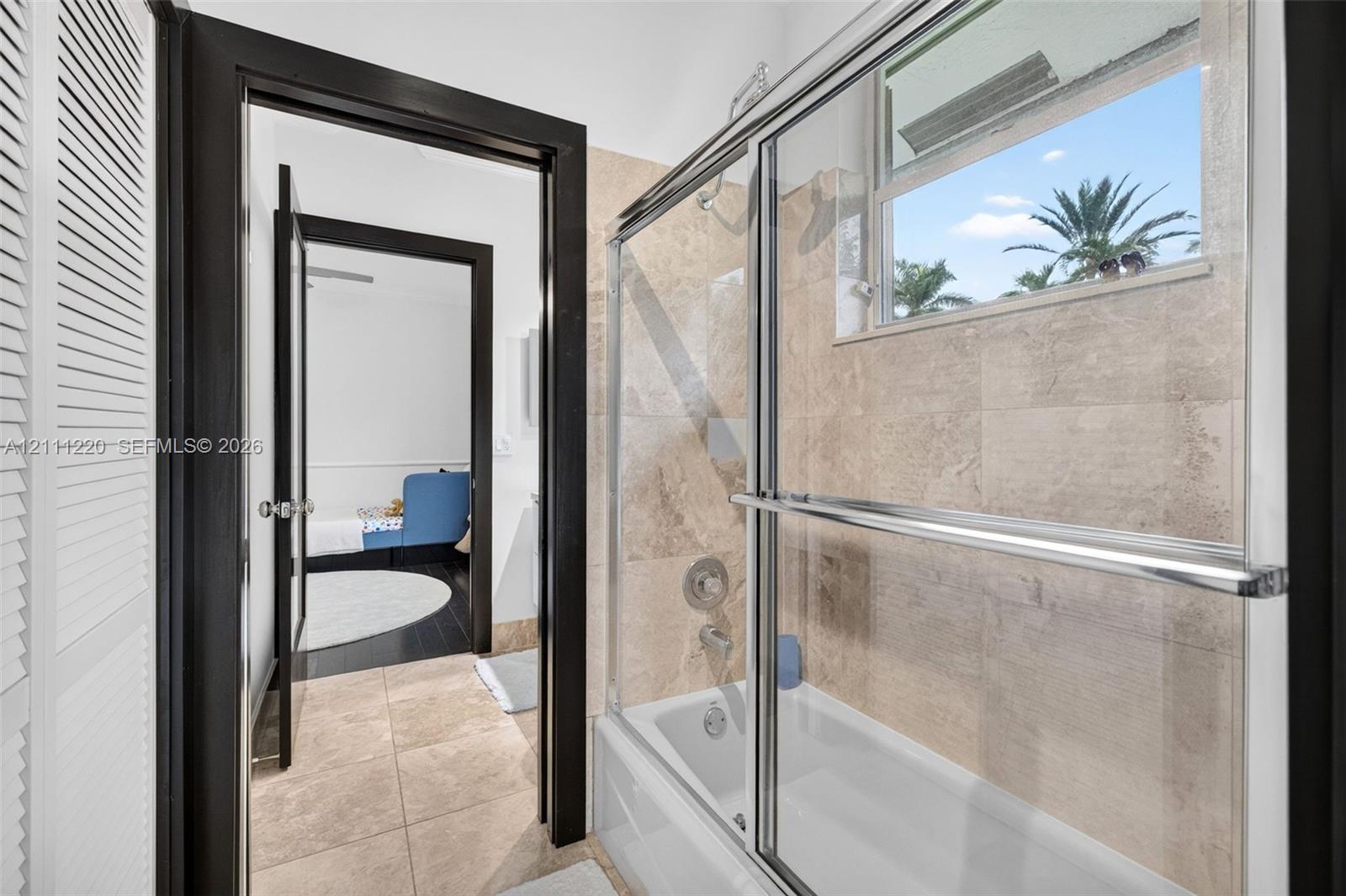 Full bathroom featuring a tub-shower combination with a sliding glass enclosure, large-format stone-finish wall and floor tiling, and dark-finished door trim
