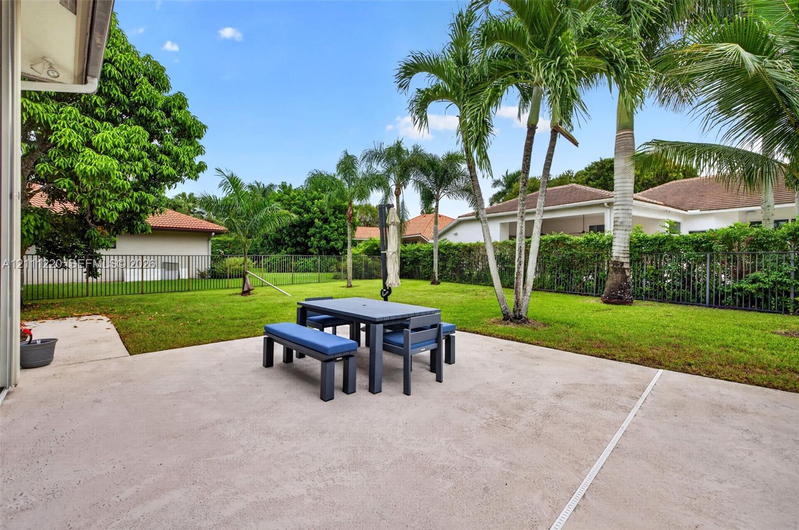 Concrete patio featuring a sodded lawn, perimeter metal fencing, and mature palm trees