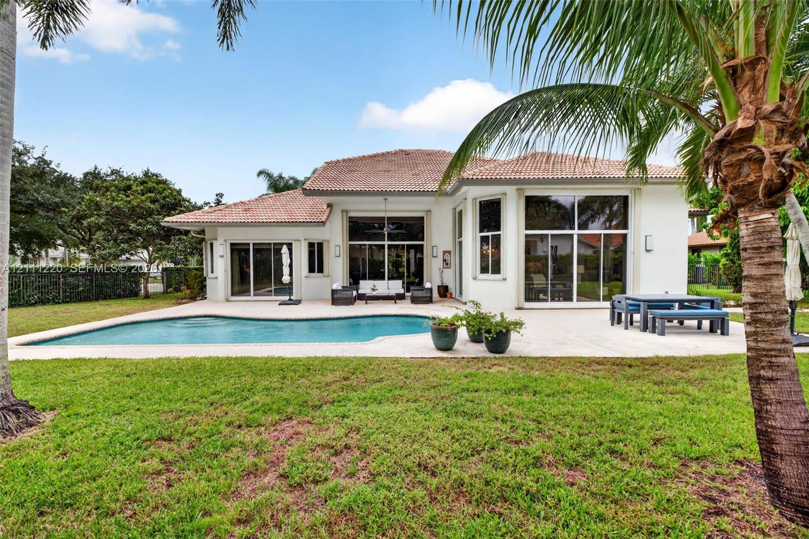 Rear exterior featuring a tile roof, stucco finish, in-ground swimming pool, concrete patio, and floor-to-ceiling glass panel doors