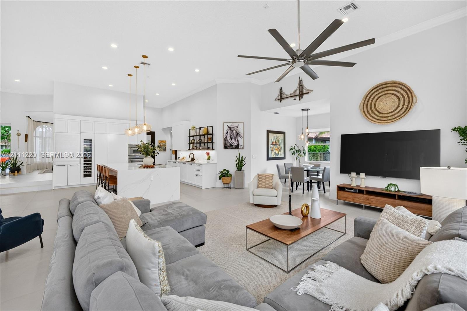Open-concept living space featuring high ceilings, a center island with waterfall-edge countertop, recessed lighting, multi-blade ceiling fan, and large-format tile flooring