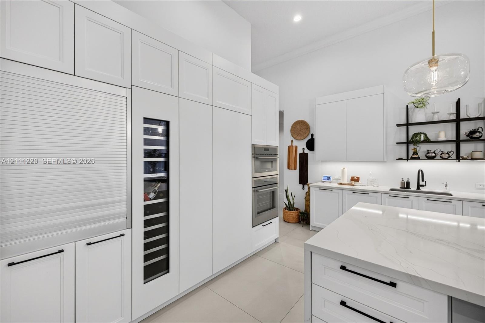 Kitchen featuring white shaker-style cabinetry, floor-to-ceiling panel-ready appliances, a built-in wine cooler, wall-mounted double ovens, and a central island with a stone-finish countertop