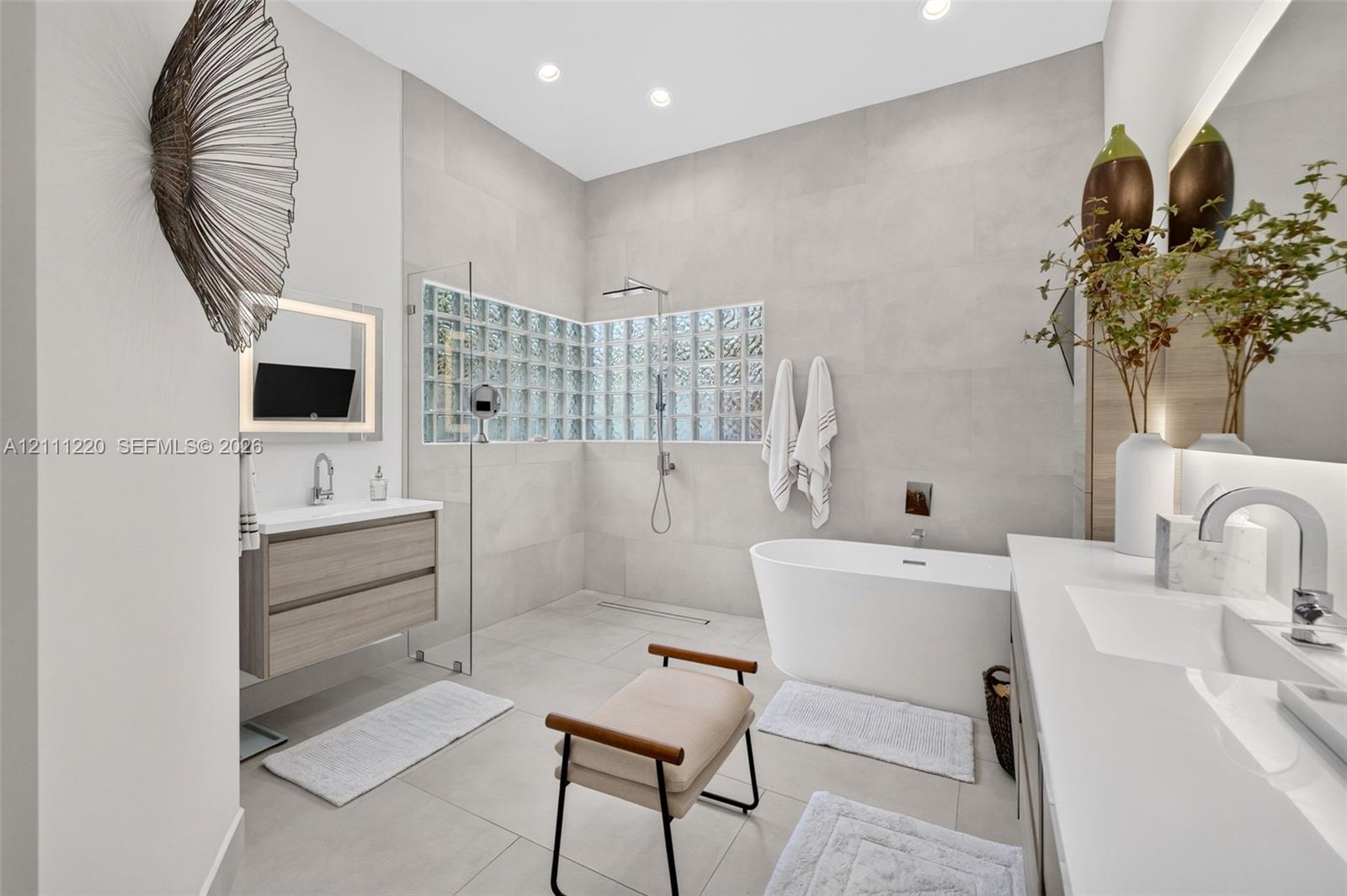 Bathroom featuring a freestanding soaking tub, glass-enclosed shower with glass block accent wall, wall-mounted wood-finish vanity, and integrated LED-lit vanity mirror