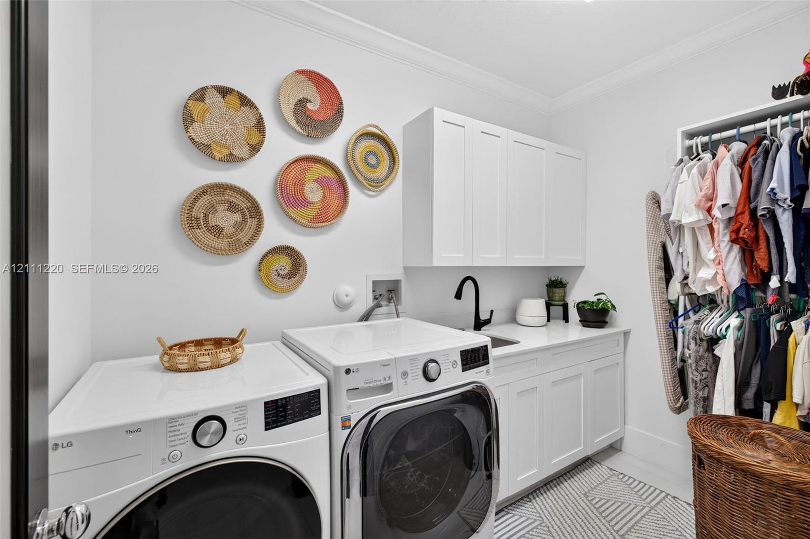Laundry room featuring shaker-style upper and lower cabinetry, white quartz countertop, undermount sink with a matte black faucet, and patterned tile flooring
